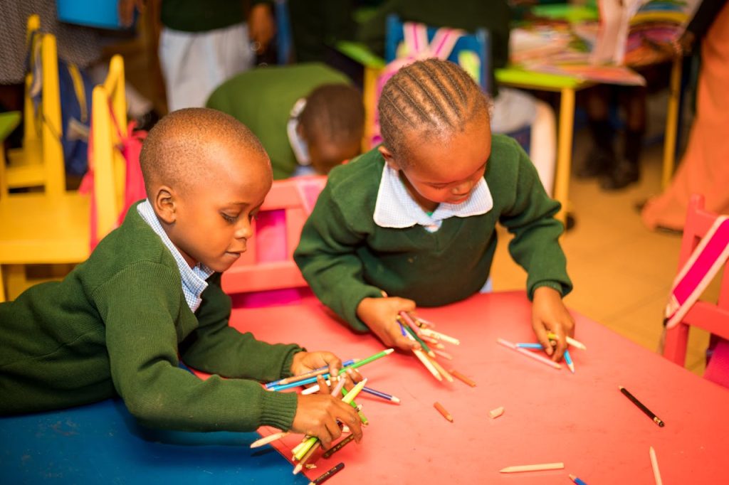 pexels photo 14621739 Two children at a table in a classroom, engaged in creative activities with colored pencils.