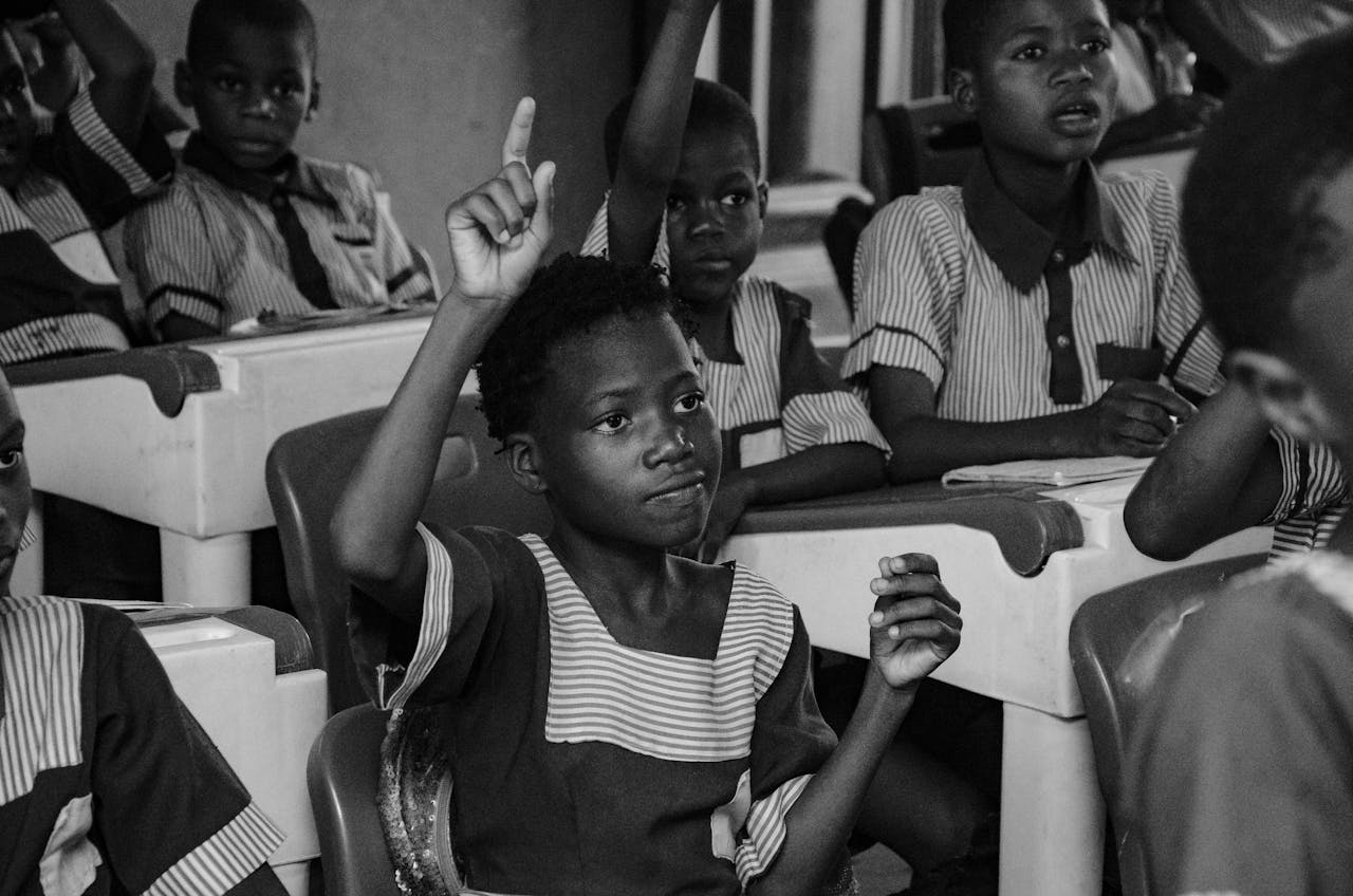 services-02 Black and white photo of students actively participating in a classroom lesson, raising hands to ask questions.