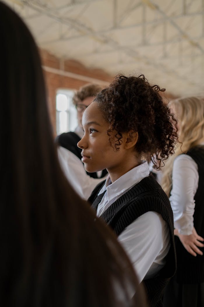 hero-img-02 Profile of a teenage girl with curly hair in a school uniform, indoors.