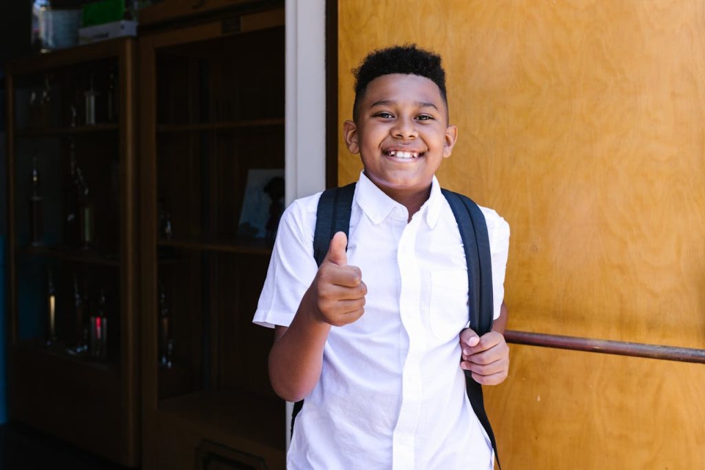 pexels photo 8499487 Smiling student with backpack giving thumbs up, standing at school entrance.