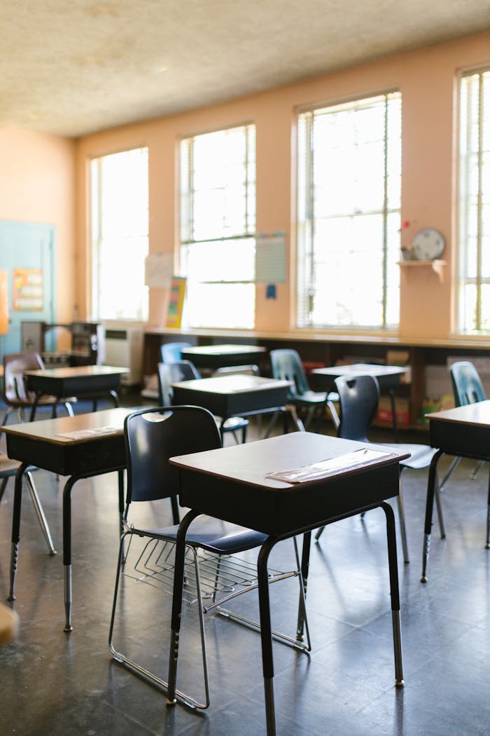 A bright, empty classroom with arranged desks and chairs, illuminated by natural sunlight.